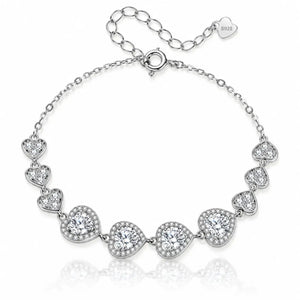 A silver-tone chain bracelet featuring seven heart-shaped settings, each adorned with clear stones, displayed on a clean white background with a soft reflection.
