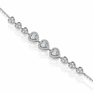 A silver-toned heart-link bracelet featuring clear heart-shaped gemstones surrounded by smaller pavé accents, displayed diagonally on a reflective white surface.