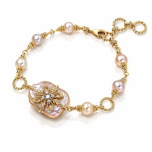 A gold chain bracelet featuring baroque pearls in soft pink and white, a large pink pearl flower centerpiece with gold filigree and clear rhinestones, and a lobster clasp, shown on a white background.