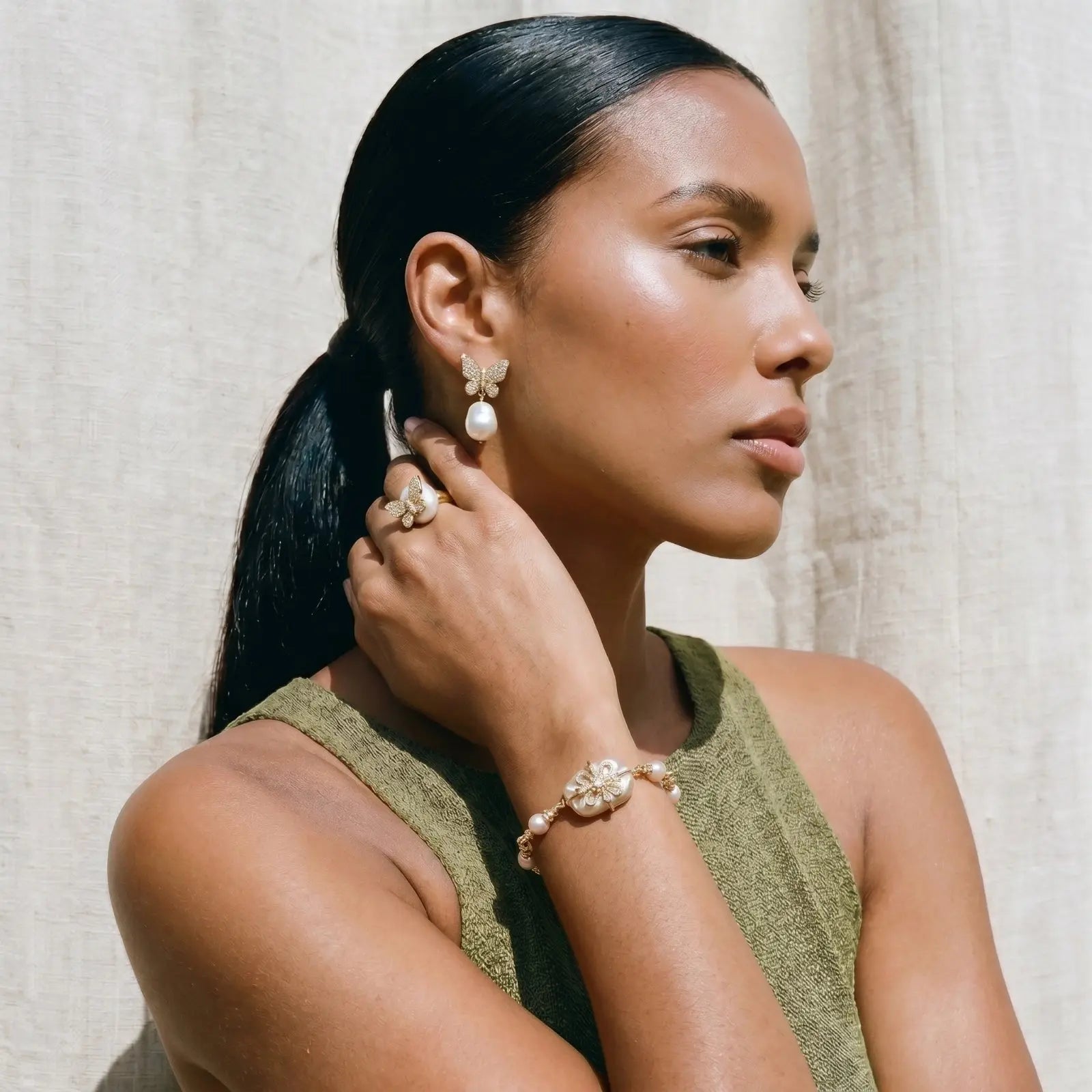 Woman wearing pearl earrings and bracelet against a neutral background