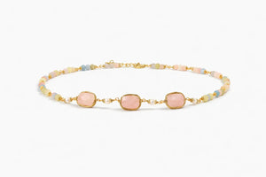 Gold bracelet with pink and blue beads on a white background