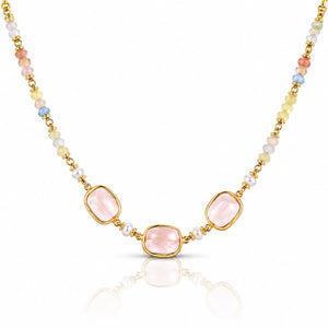 A gold-tone beaded necklace featuring three central light pink rectangular gemstones, flanked by small white pearls and multicolored beads in pastel shades of yellow, blue, and peach, set against a clean white background with a soft reflection below.