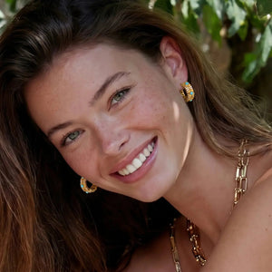 Woman with gold earrings and necklace against a natural background