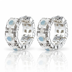 A pair of silver huggie hoop earrings decorated with white mother-of-pearl flower petals, clear rhinestones, and light blue oval center stones, displayed on a reflective white surface.