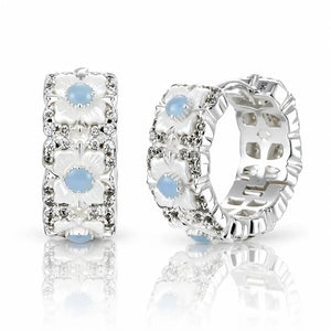 A pair of silver-toned hoop earrings with white floral enamel details, clear rhinestone accents, and light blue oval gemstones, displayed on a reflective white surface.