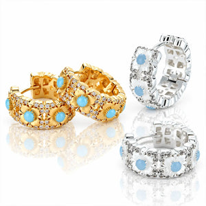 Three pairs of hoop earrings shown on a clean white reflective background: two gold-toned and one silver-toned, each featuring white floral shapes, clear stones, and light blue oval centers.