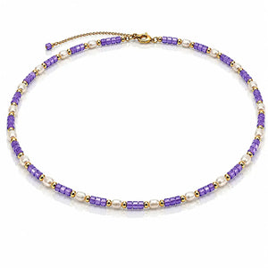 A beaded necklace featuring alternating strands of purple cylindrical beads and white pearl-like beads, separated by small gold spacer beads, with a gold clasp and extender chain on a white background.