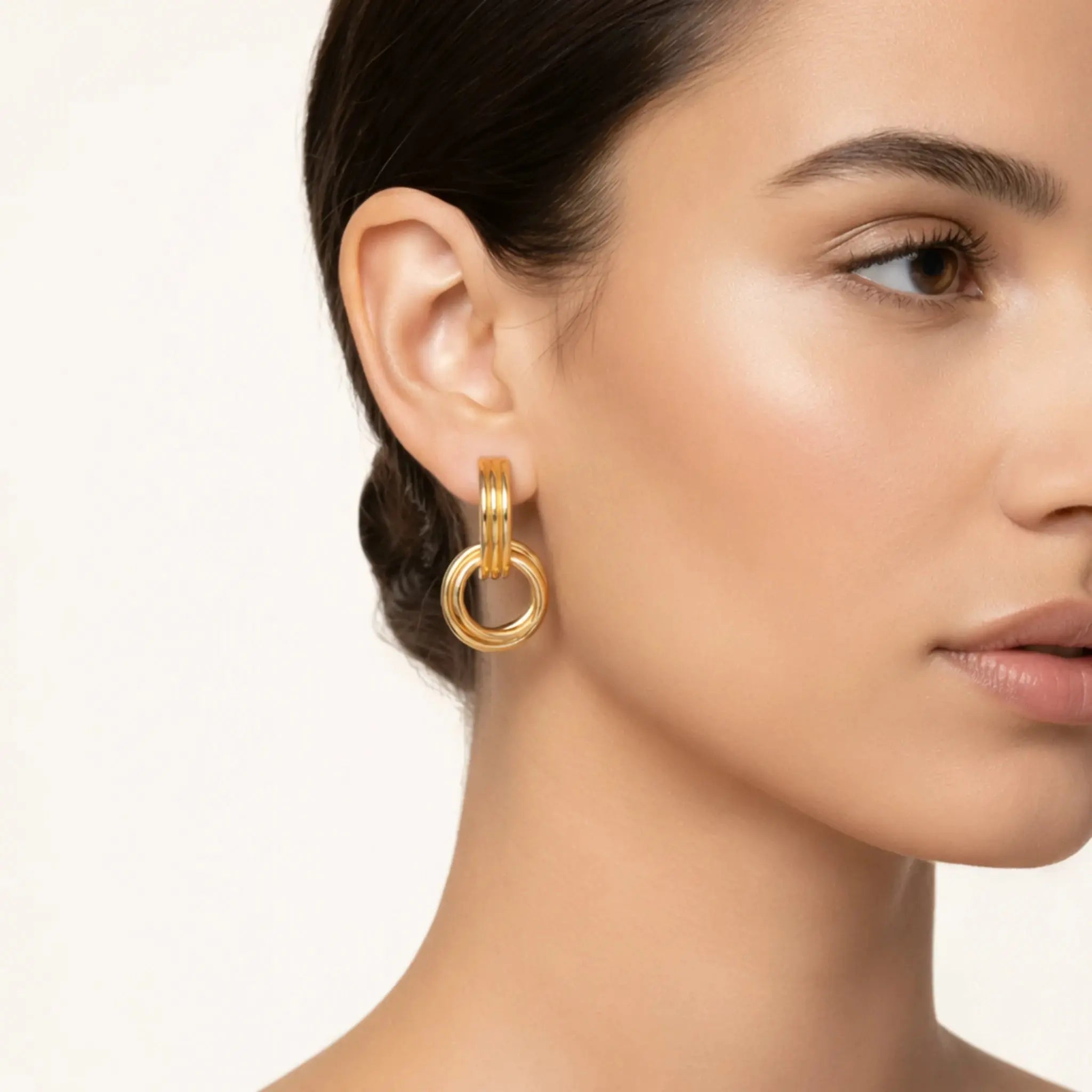 Woman wearing 18K gold-plated linear loop earrings, close-up on ear and jewelry.