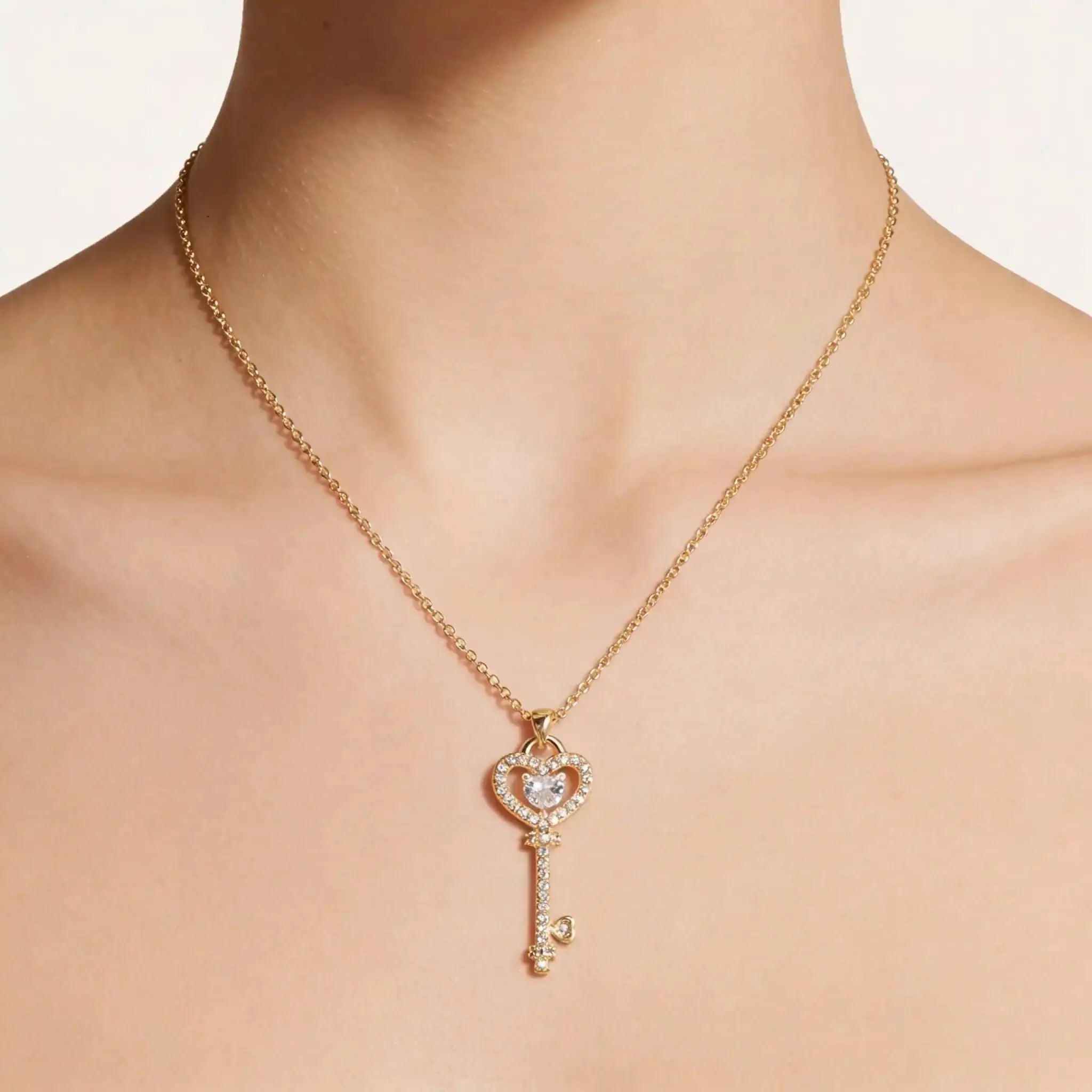 Gold necklace with a heart-shaped key pendant on a plain background