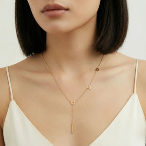 Woman wearing a gold necklace with a white top on a neutral background