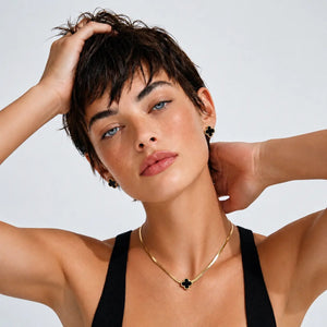 Woman with short hair wearing a black top and gold necklace against a light background