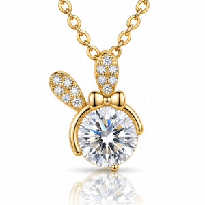A gold pendant necklace featuring a bunny-shaped charm with a large round clear center stone and smaller clear stones along the ears and bow, shown on a white background with a soft reflection below.