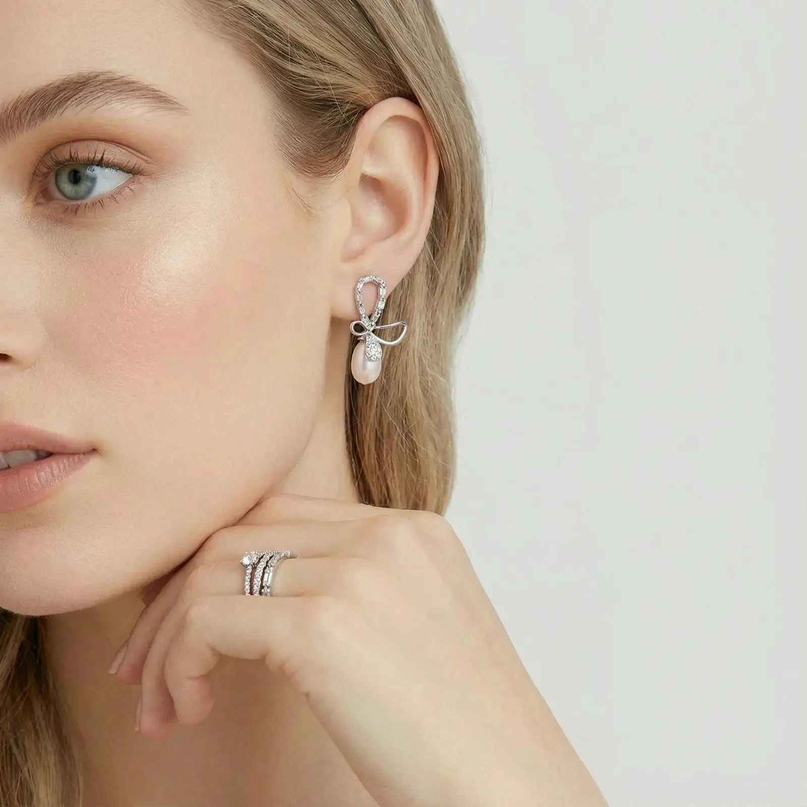 Woman wearing bow-shaped pearl drop earrings and stacked diamond rings