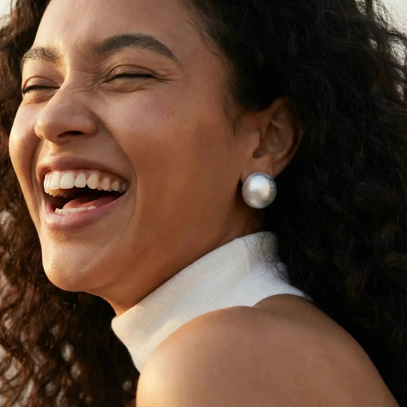 Woman wearing large brushed 925 sterling silver dome clip earrings, smiling outdoors