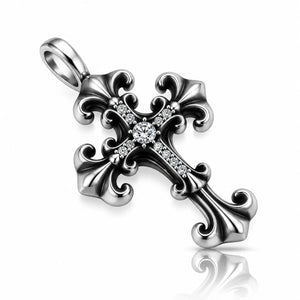 A silver-toned ornate cross pendant with a central round clear gemstone and small clear stones along the arms, shown on a white background with a soft reflection below.