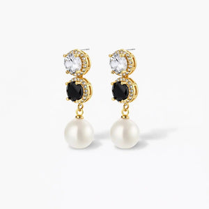Gold drop earrings with clear and black gemstones and round pearl dangles on white background