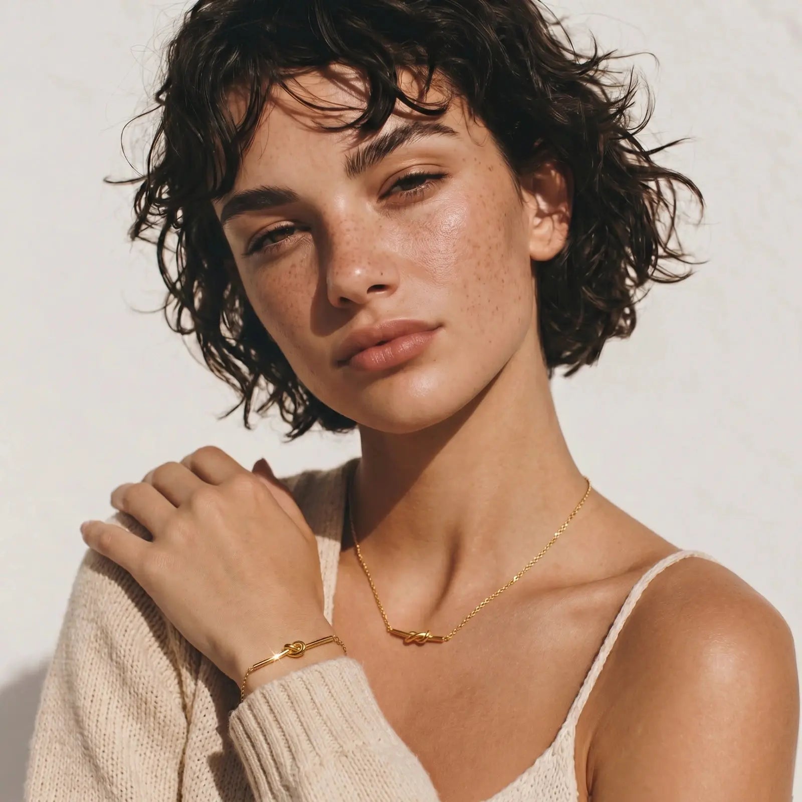 Woman wearing a gold necklace and bracelet against a plain background