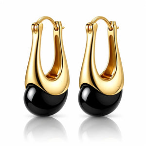 A pair of gold and black drop hoop earrings with a polished gold-tone curved upper section and a glossy black spherical drop below, shown on a white background with a soft reflection.