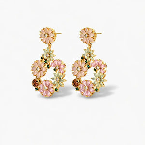 Gold floral earrings with pink and white flower details on a plain background