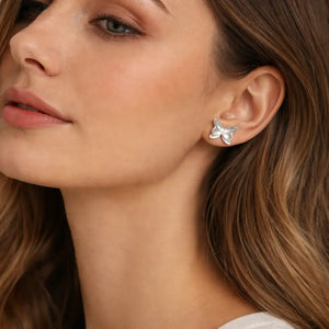 Close-up of a woman wearing silver butterfly earrings with a neutral background