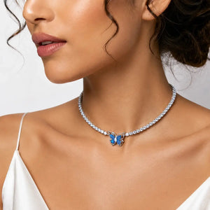 A close-up of a woman wearing a delicate silver-toned choker necklace adorned with clear stones and a small blue butterfly pendant.