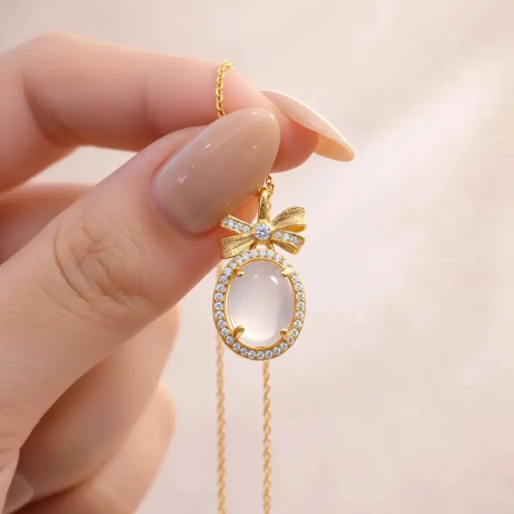 Gold necklace with a bow and gemstone held by a hand against a soft background
