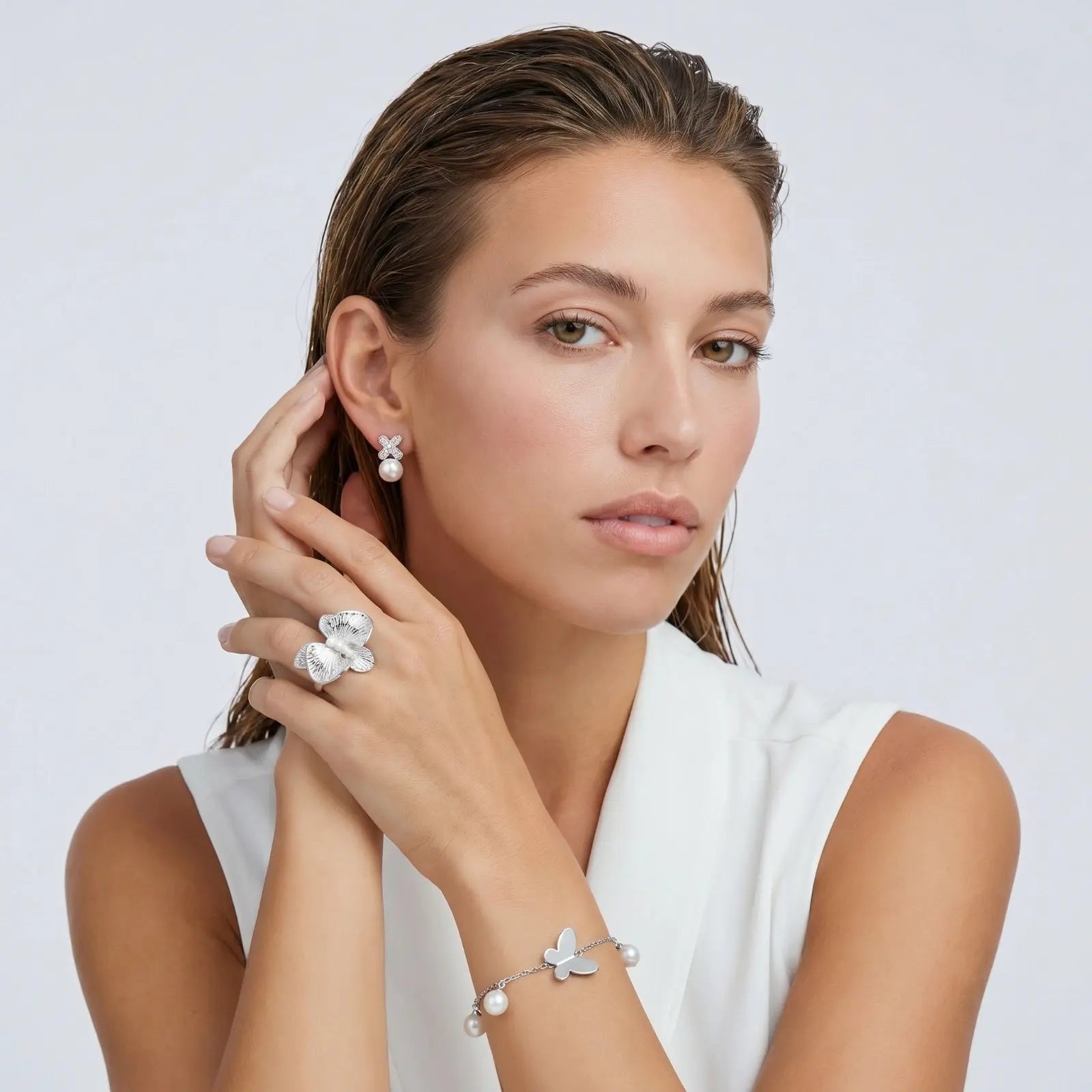 Woman wearing silver jewelry including earrings, ring, and bracelet on a white background