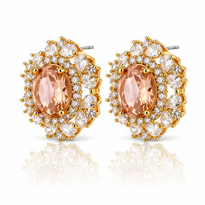 A pair of gold-plated oval stud earrings featuring a central peach-colored marquise-cut gemstone surrounded by a double halo of clear round and oval cubic zirconia stones, shown on a white background with a soft reflection.