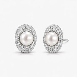 Elegant oval pearl stud earrings with double halo of sparkling pave stones on white background.