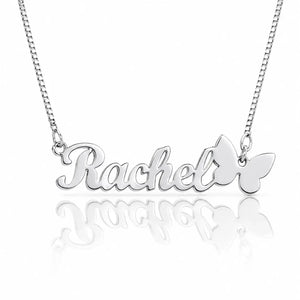 A silver nameplate necklace spelling 'Rachel' in cursive, with a butterfly pendant on the right side, suspended from a silver chain against a white background with a soft reflection below.