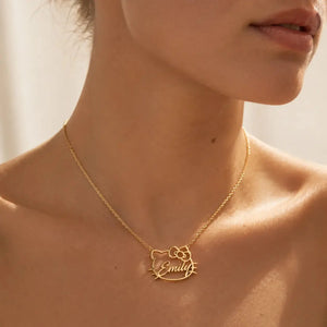 A close-up of a model wearing a delicate gold chain necklace with a custom name pendant that reads 'Emily' inside a Hello Kitty-inspired cat face outline.