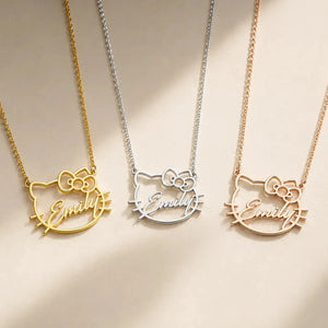 Three custom name necklaces with a Hello Kitty cat face outline pendant spelling 'Emily' are displayed on a warm beige background. The necklaces are shown in three metal finishes: gold, silver, and rose gold.