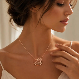 A woman wearing a delicate rose gold necklace with a custom name 'Emily' in script inside a Hello Kitty face outline pendant, shown in a warm, close-up lifestyle shot.