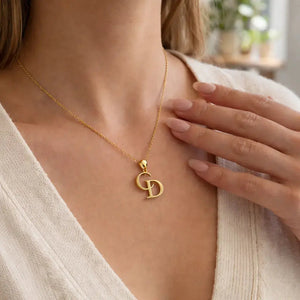 Gold necklace with a pendant worn by a person, with a blurred indoor background.