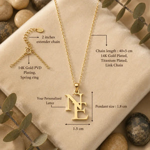 Gold personalized letter necklace with an 'NE' initial pendant, displayed on a beige fabric background with decorative stones and eucalyptus leaves. The image includes detailed dimension annotations and a separate inset showing the spring ring extender chain.