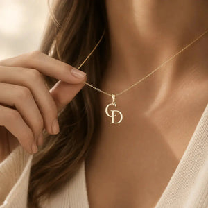 A close-up lifestyle shot of a model wearing a delicate gold necklace with a double 'D' initial pendant, with her hand gently touching the chain.