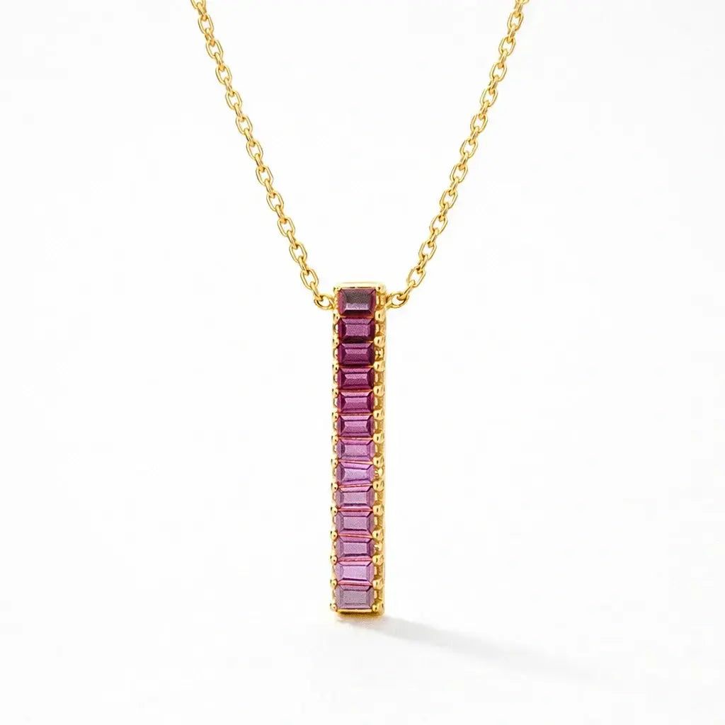 Gold chain necklace with vertical pink baguette bar pendant on white background