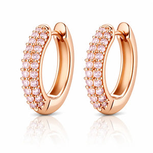 A pair of rose gold huggie hoop earrings adorned with rows of small pink cubic zirconia stones, displayed on a clean white background with a soft reflection below.