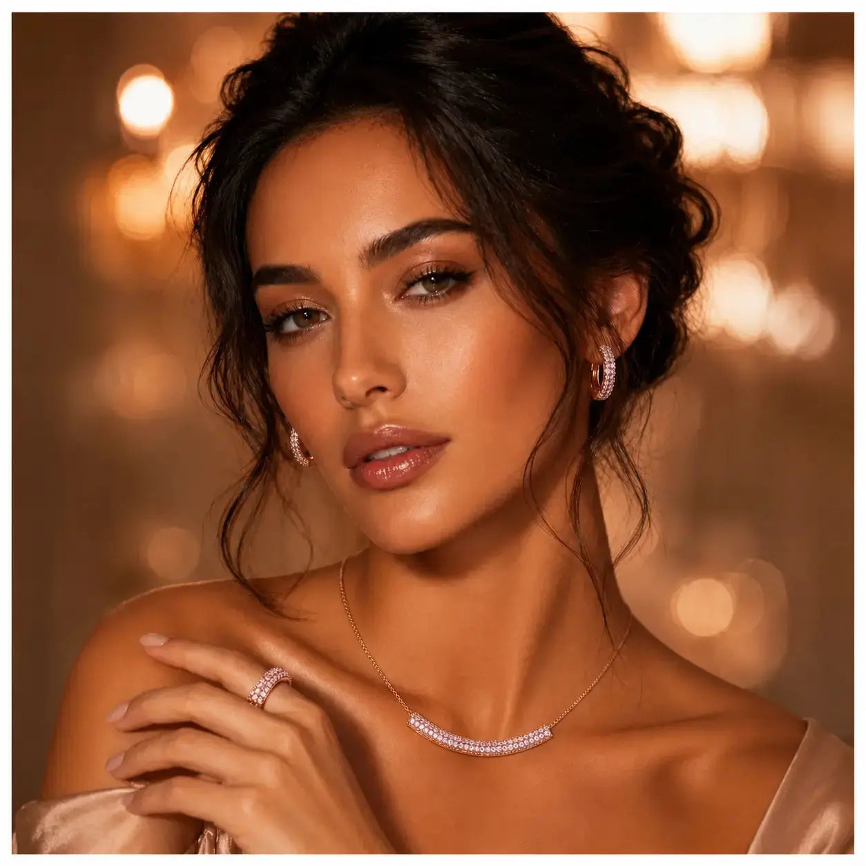 A close-up portrait of a woman wearing a delicate silver necklace with a curved pavé-style centerpiece, matching drop earrings, and a ring, set against a warm, softly blurred bokeh background of golden lights.