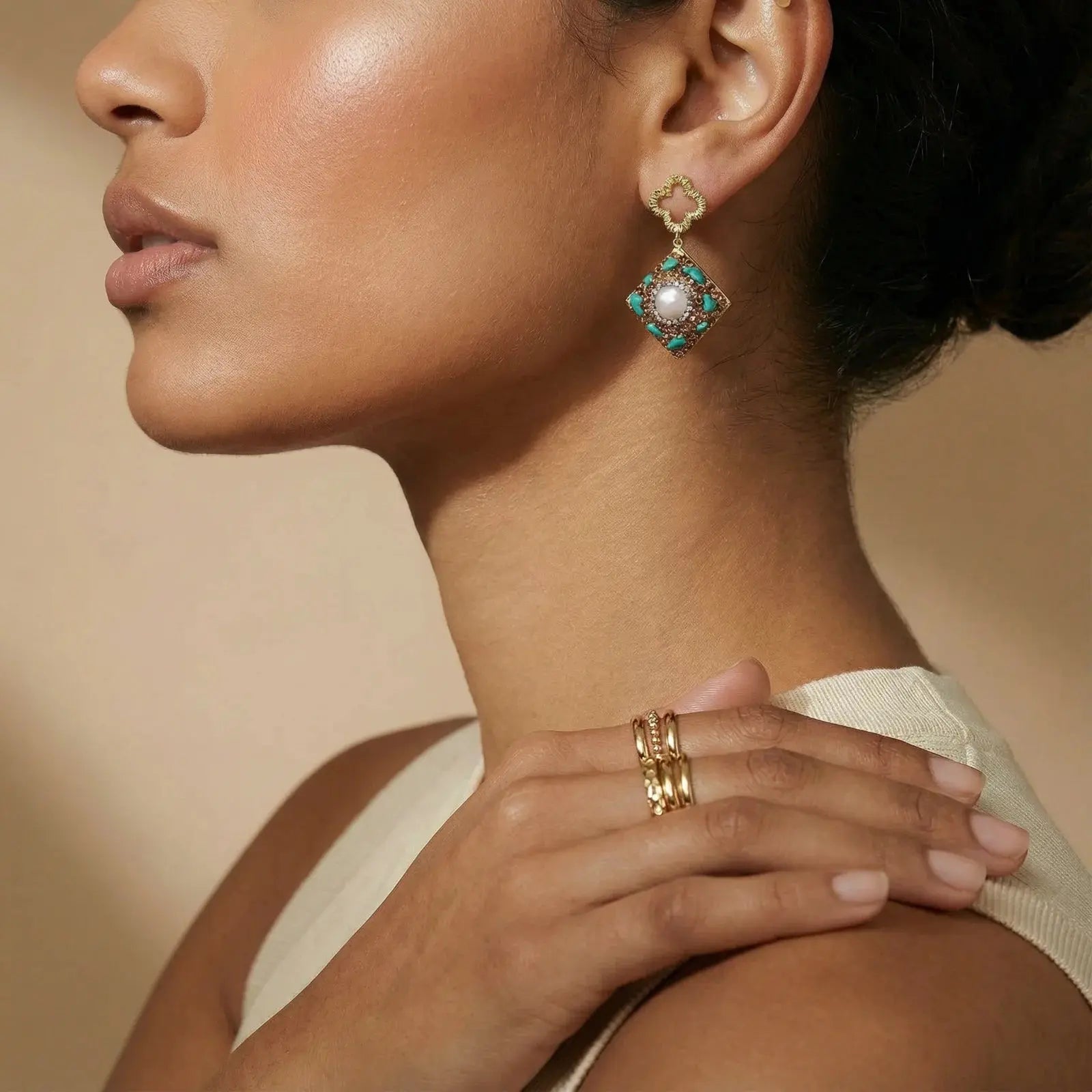 Close-up of a woman wearing gold earrings and rings with a neutral background