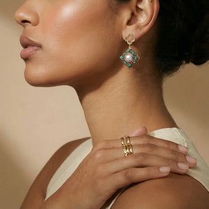Close-up of a woman wearing gold earrings and rings with a neutral background