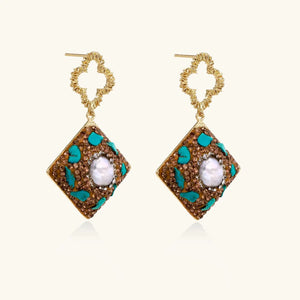 Pair of gold earrings with diamond-shaped design and central pearl on a white background