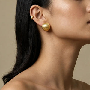 Close-up of a person wearing gold earrings with a neutral background