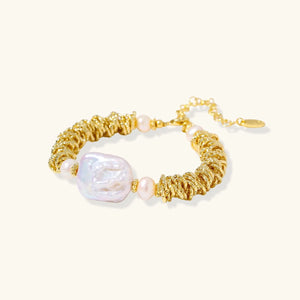 Gold bracelet with large pearl and smaller beads on a white background