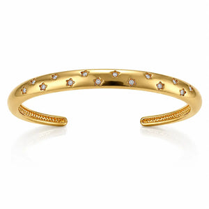 A polished gold open cuff bracelet decorated with small star-shaped settings holding clear round stones, shown on a clean white background with a soft reflection below.