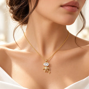A close-up lifestyle shot of a model wearing a delicate gold pendant necklace. The pendant features a small gold figure adorned with clear crystals, which are excluded from the color analysis according to the rules.