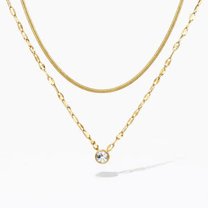 Layered gold necklaces with a solitaire crystal pendant on a white background