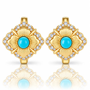 A pair of gold flower-shaped earrings with turquoise blue center stones and clear accent stones, shown on a white background with a soft reflection below.