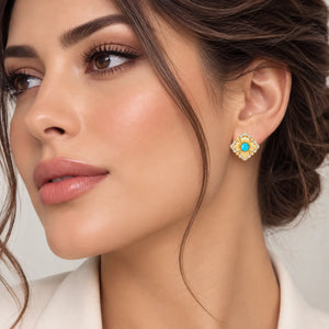 A close-up of a woman wearing a gold-toned floral stud earring with a turquoise blue center stone and small clear accent stones.