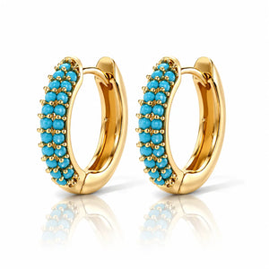 A pair of gold huggie hoop earrings embellished with rows of small turquoise blue stones, displayed on a clean white background with a soft reflection below.